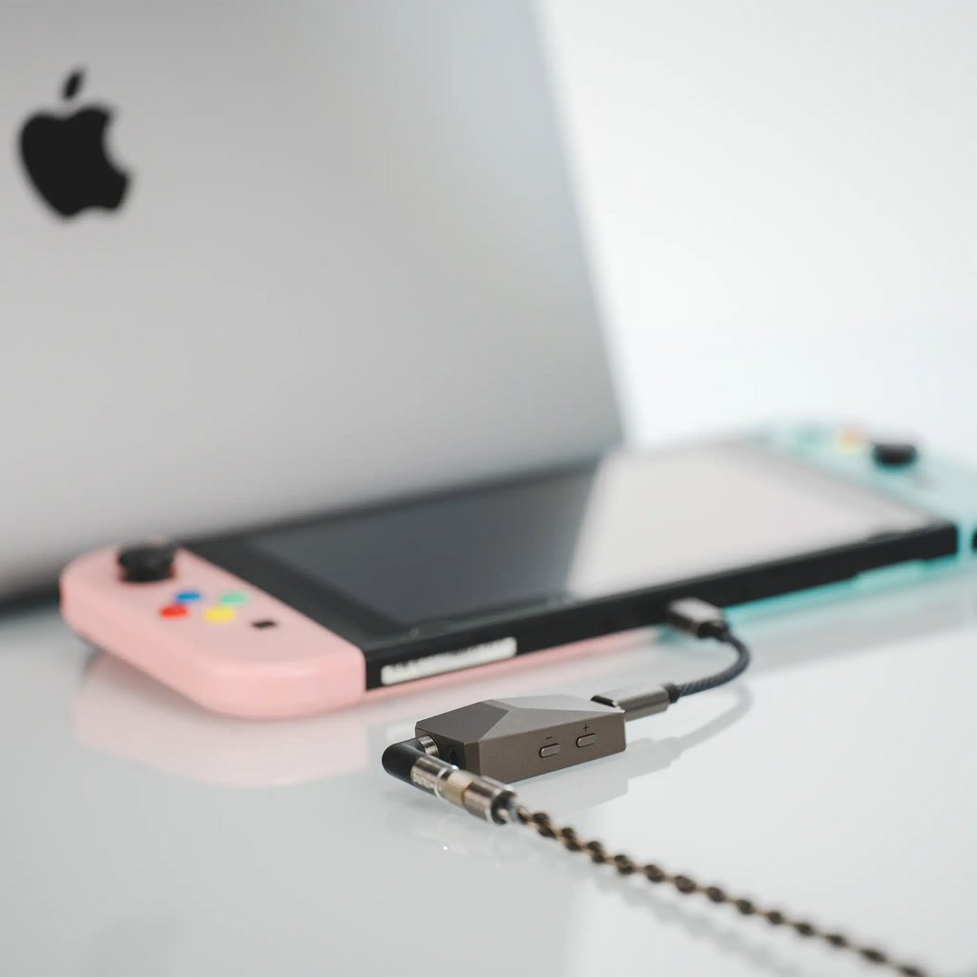DUNU DTC 480 DAC and amp laying on glossy table plugged into pink and blue Nintendo switch with laptop