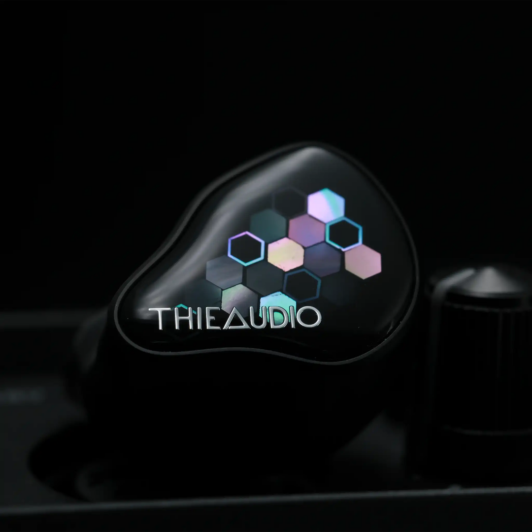Thieaudio Monarch MKIV IEM with Kaleidoglow faceplate sitting front center on black desktop amp